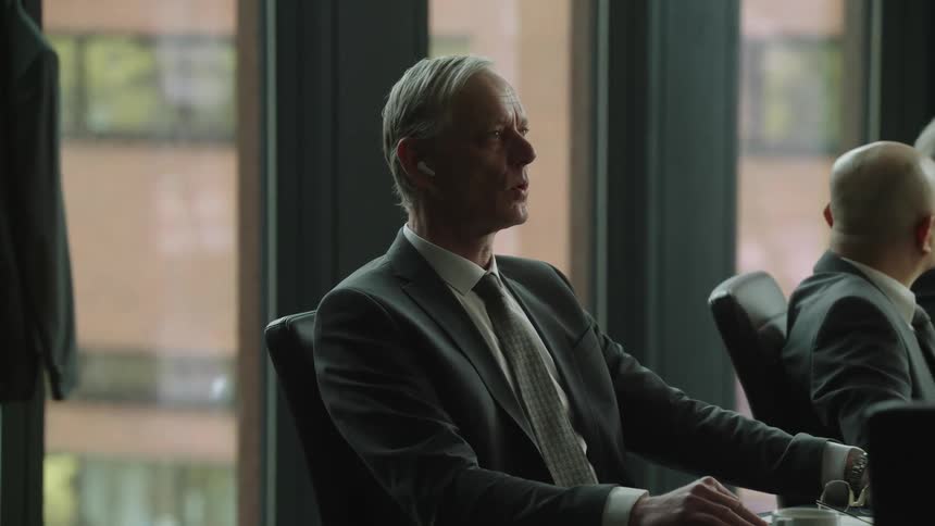 Business man wearing earbuds attends a board meeting in the office looking around lost in tought