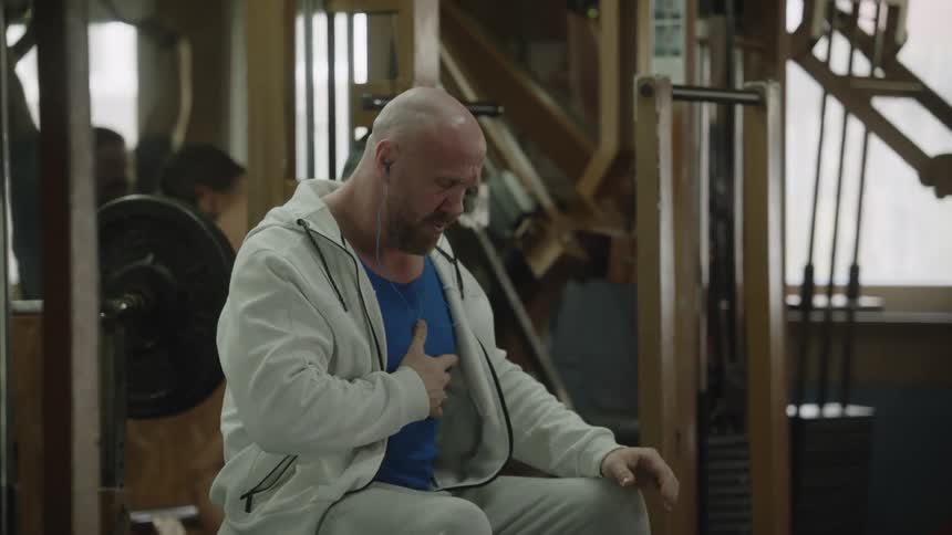 A large bald man concentrates before laying back to lift weights