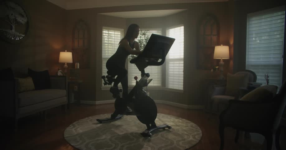 Woman with black top and leggings rides stationary bike in the living room