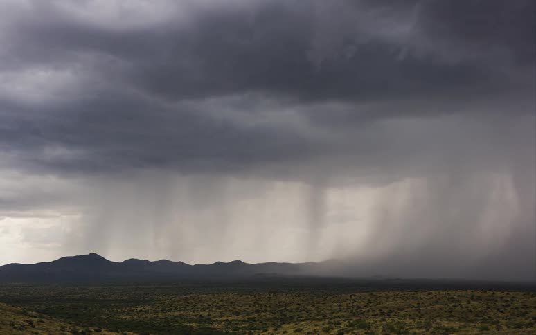 A storm passes over a field and some mountains