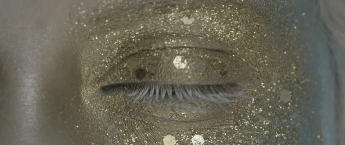 A person blinks with gold glitter on their eye
