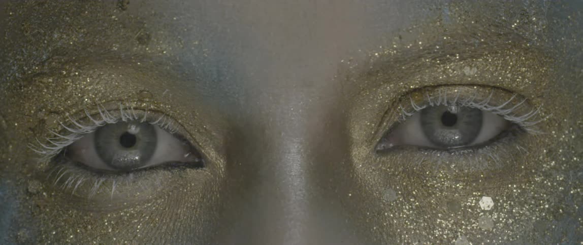 Blue eyes surrounded by white mascara and gold glitter makeup