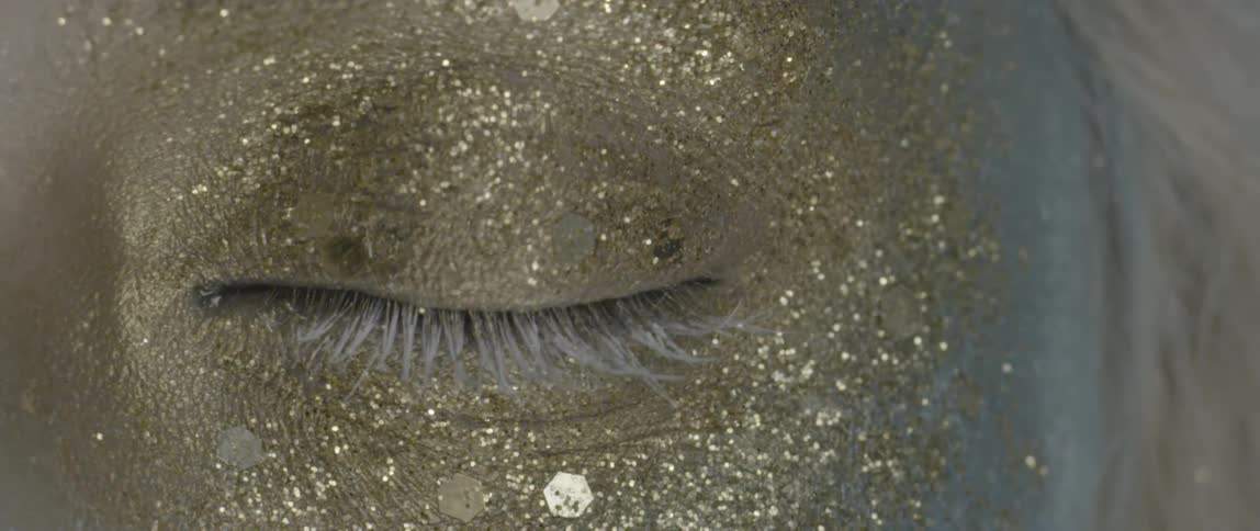 A person blinks with gold glitter around their eye