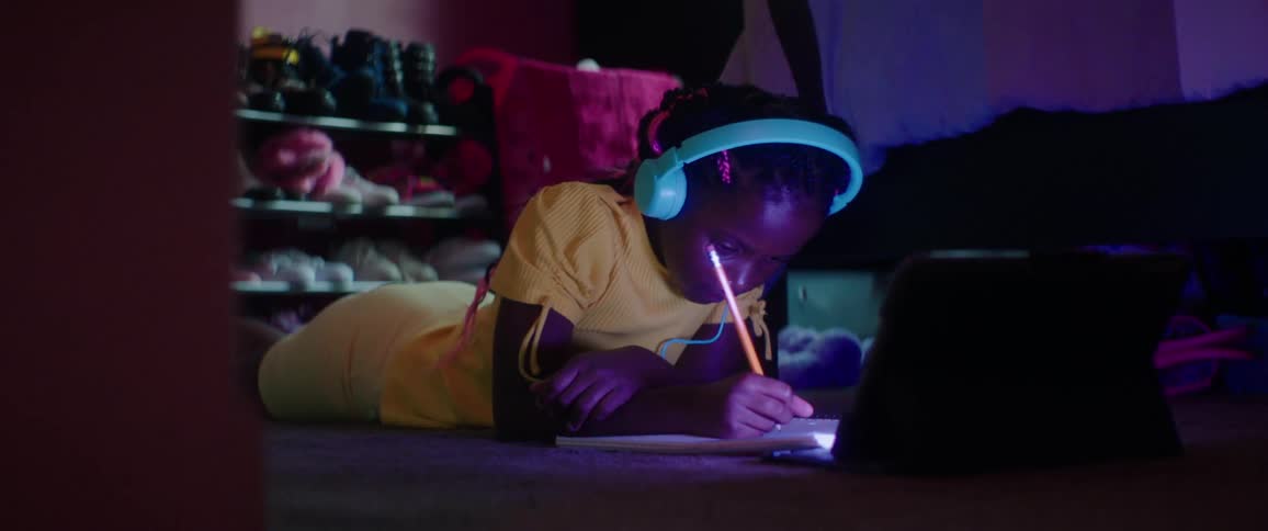 Girl lies on floor taking notes while listening and watching tablet