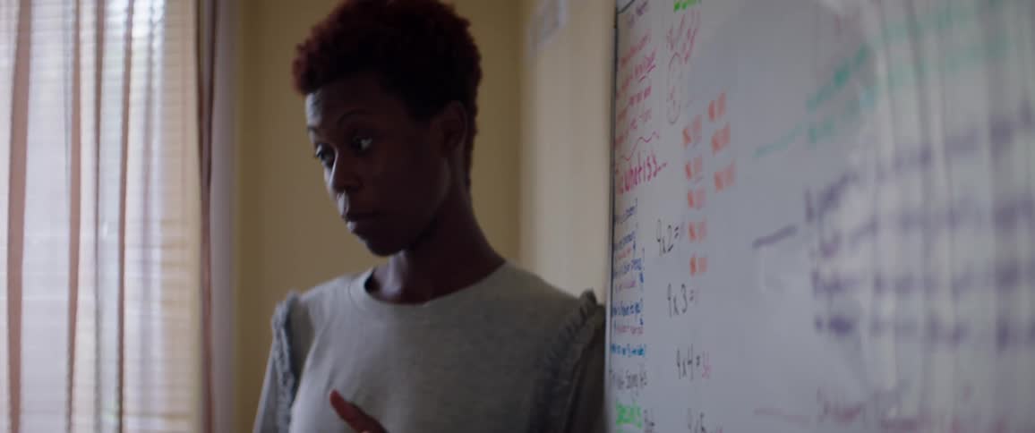 Black woman stands near a whiteboard as she teaches