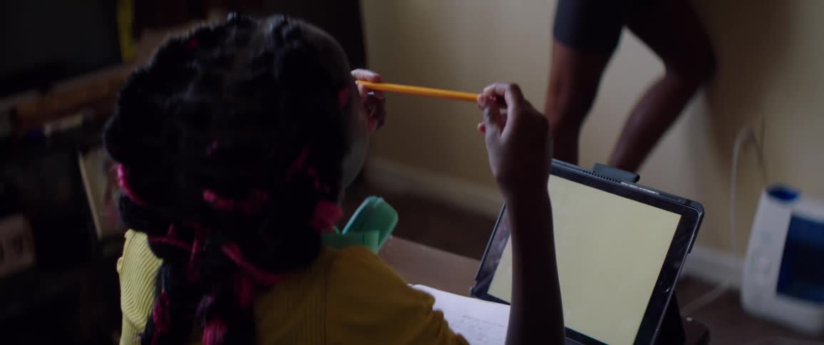 A girl with a pencil sitting on a chair in front of a desk in front of a laptop