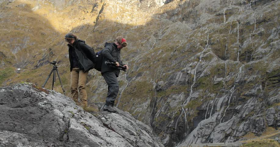 Two people pack up their a camera equipment on rocks