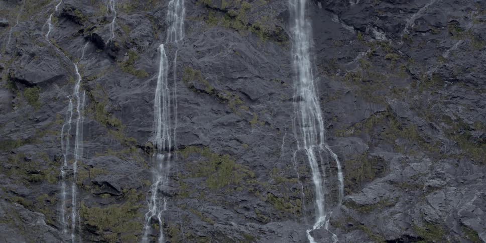 Water pours down three spots of a cliff