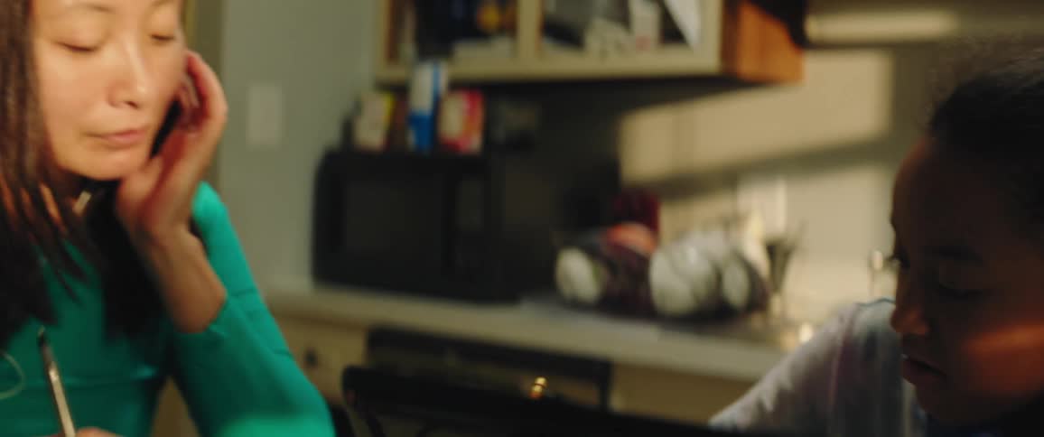 A woman is helping a girl with school work in the kitchen