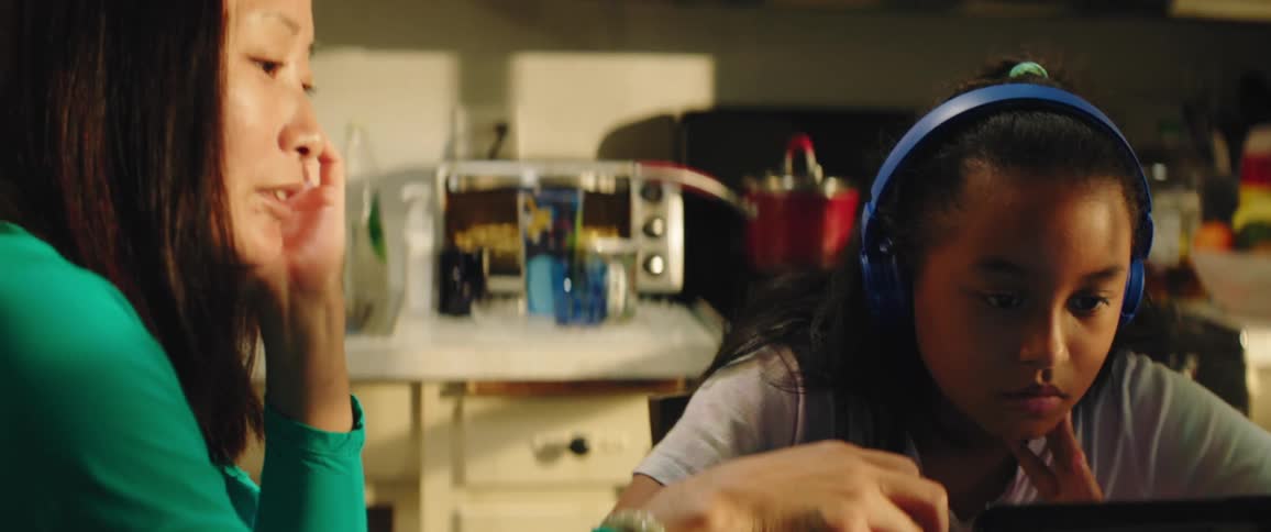 A woman and her daughter sit in the kitchen with a laptop doing school work