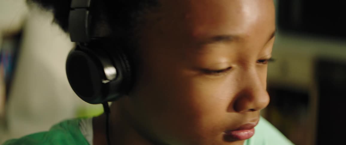 Black little girl sitting at the table wears black headphones in the kitchen