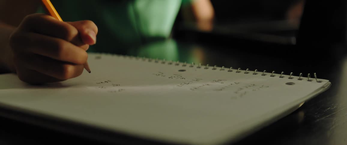 Black girl sitting at a desk writes in a notebook with a pencil