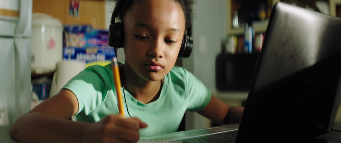 A young girl sits in front of her laptop at home and does school work