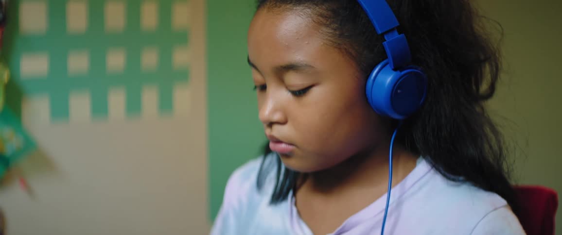 Black child wearing blue headphones and sitting at a desk uses a laptop to study at home