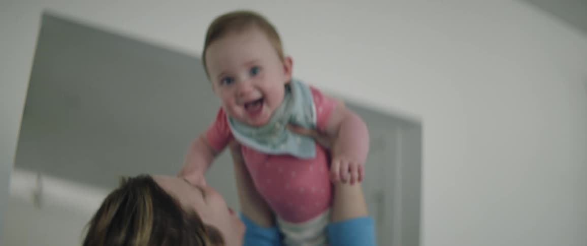 A woman holds her baby in the air and kisses her as the baby smiles she gives her a hug