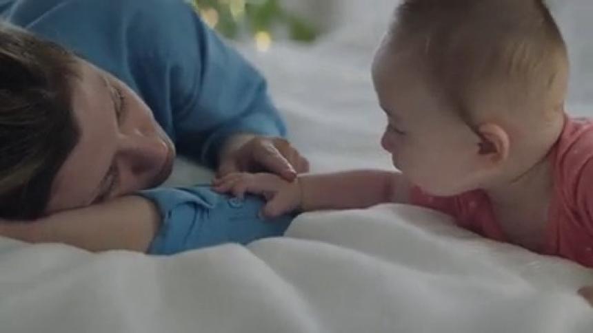A mother plays with a baby on a bed caressing their head and hand