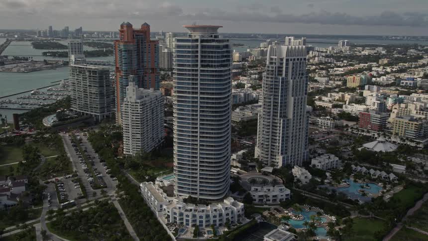 Aerial footage of modern skyscrapers towering near the beach in South Beach Miami with sunbathers and beachgoers enjoying the seaside