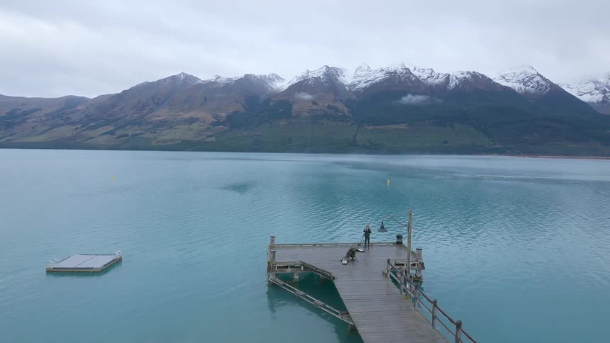 Photographers setting up at the end of a pier near snow-capped mountains