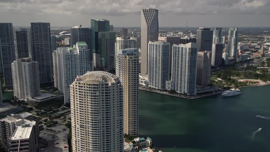 Aerial flyby of Brickell Key skyscrapers and Downtown Miami revealing the Miami River cutting through the citys downtown area with partly cloudy skies