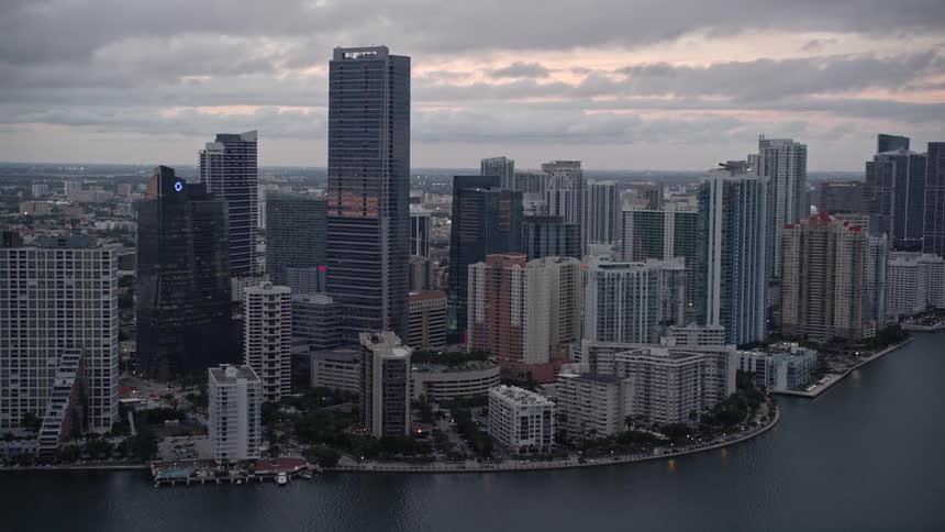 Approaching a bustling Downtown Miami skyscrapers and high-rise hotels dot the shoreline as the sun sets in a cloudy sky