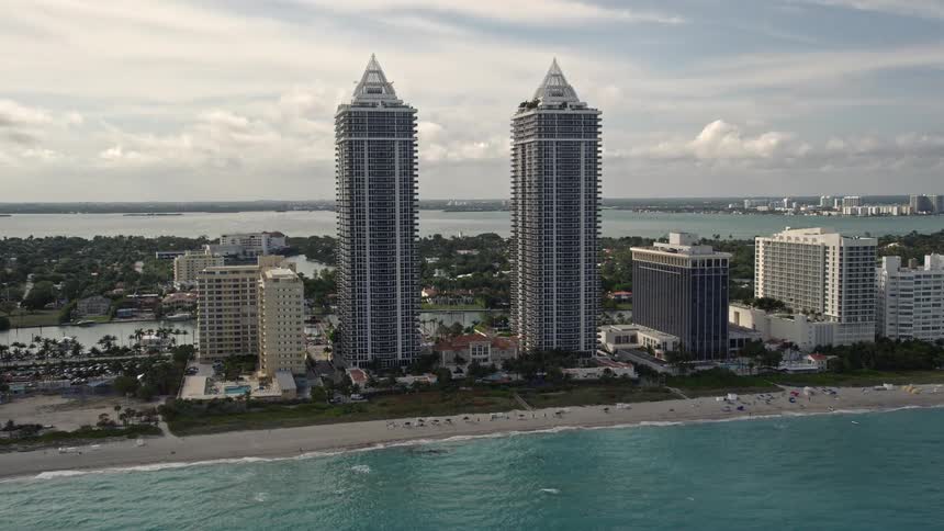 Approaching Miami Beachs oceanfront two matching skyscrapers dominate the skyline as sunbathers and beach-goers relax on the shoreline below