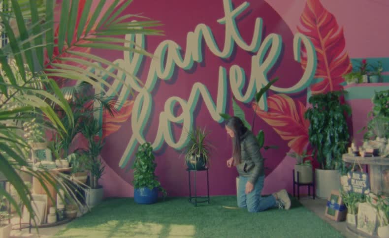 Woman kneels near plant store mural and adjusts potted plant on plant stand