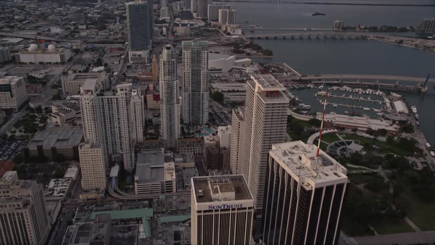 A spectacular aerial view of the towering skyscrapers of Downtown Miami at sunset as the camera tilts up from a metropolis beneath and approaches the stunning buildings