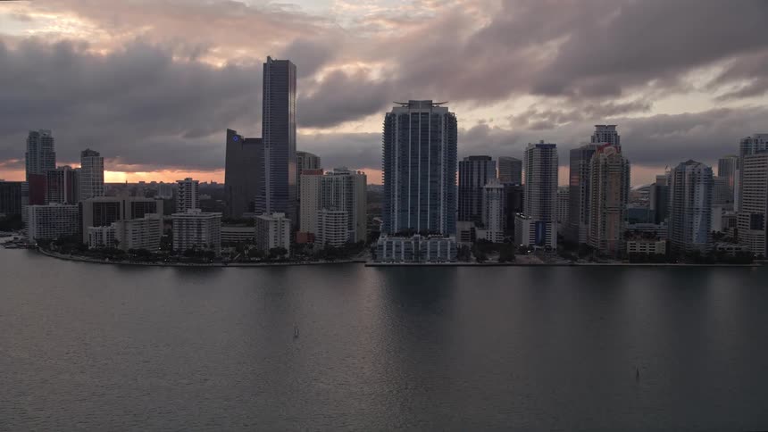 Aerial footage of Downtown Miami skyline as it is revealed and approached during sunset featuring high-rise buildings and hotels along the coastline of Florida