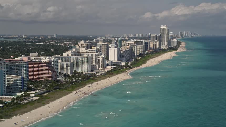 Aerial footage revealing beachfront condos in Miami Beach Florida as the shot tilts up from the ocean capturing the shoreline scattered with sunbathers and other beachgoers