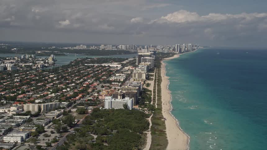 Aerial footage of Miami Beach and the town of Surfside Florida reveals coastal hotels and residential areas as the camera tilts up from beachfront homes and parks