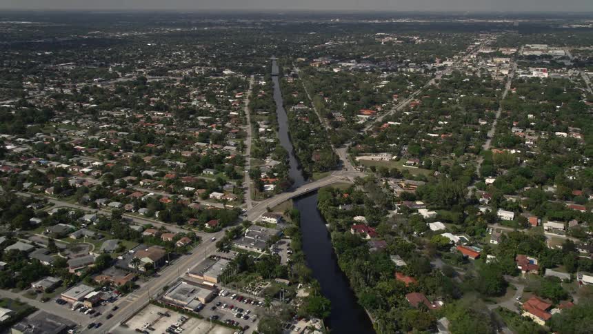 Aerial footage of a suburban neighborhood in Biscayne Park Miami Florida with a canal flowing beside a school and single-family homes