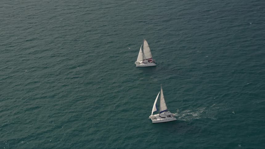 Two catamarans approach and orbit each other in the calm waters near South Beach Florida while captured in stunning aerial footage