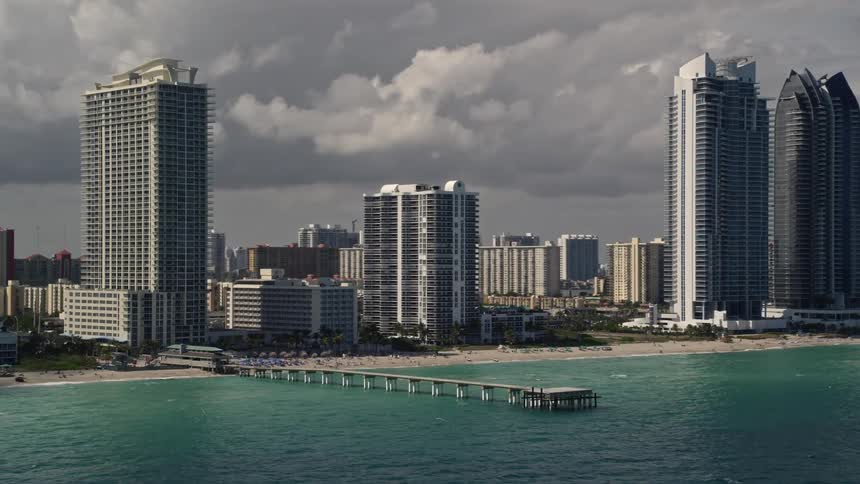 Aerial footage captured of the skyscrapers and shoreline along a populated beach in Sunny Isles Beach Florida on a cloudy day