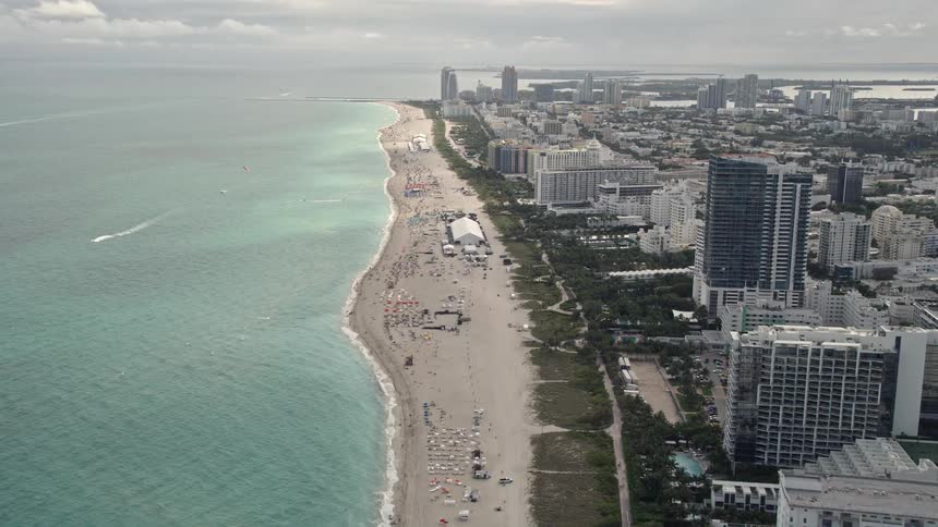 Aerial flyover captures Miami Beachs oceanfront hotels and condos with a crowded beach in view