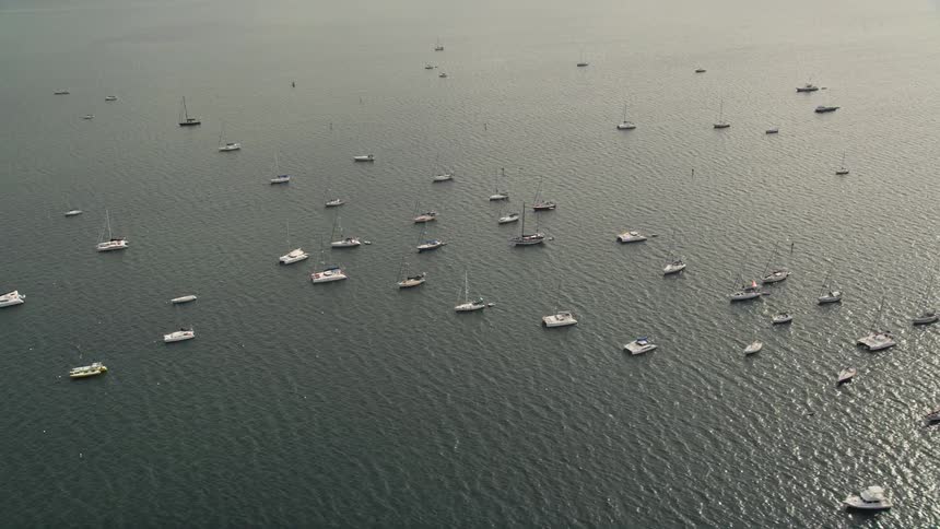 Sailboats and catamarans anchored near Coconut Grove Florida are shown from an aerial approaching and flying past them