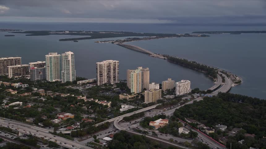Aerial footage of waterfront condo complexes the Rickenbacker Causeway and Downtown Miami at sunset highlighting its coastal beauty and metropolitan areas in Southern Florida