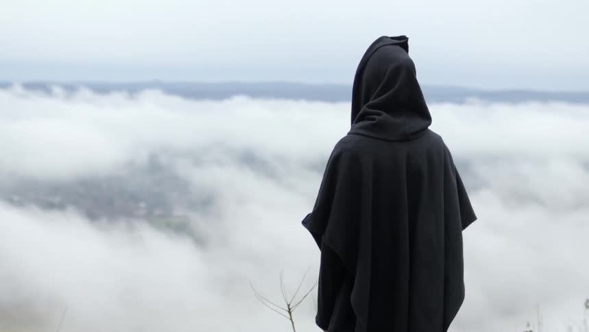 A hooded figure looks out over clouds covering a valley