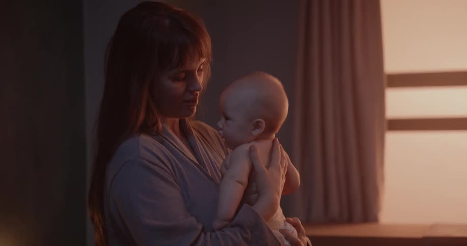 A mother is standing in a bedroom while holding her infant daughter in her arms