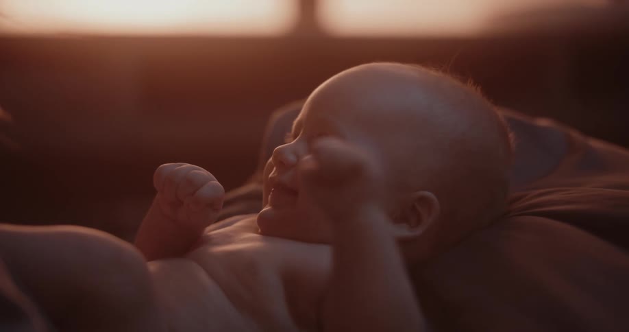Mother with brown hair holds baby in her lap laughing in room