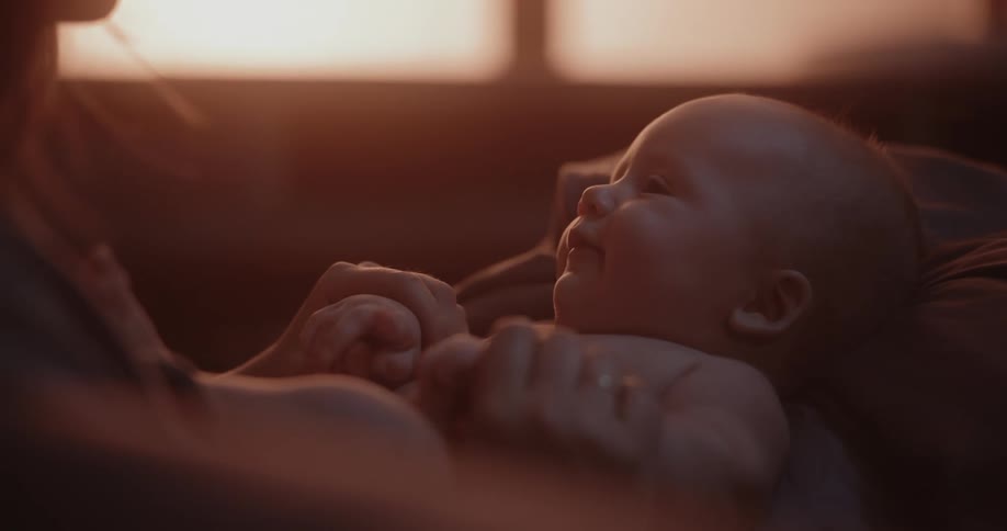 Infant baby lies in mothers lap in room while the sun shines through windows