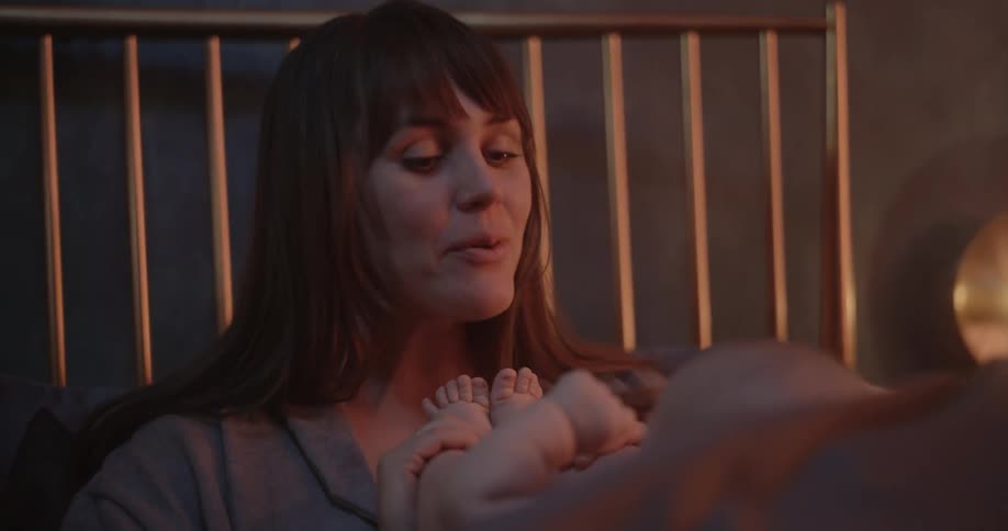 Mother with brown hair kisses feet of newborn baby laughing in bedroom