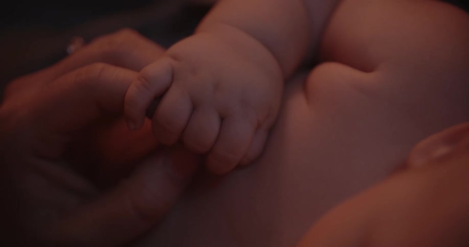 An adult hand is gently holding the hand of a baby