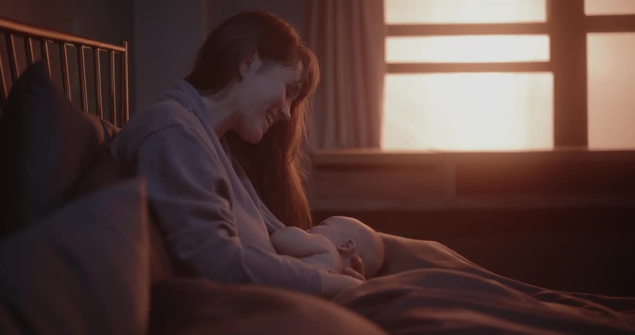 A woman coos at her baby while holding it in bed
