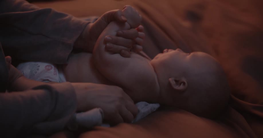 Mother puts clothes on baby with diaper in bedroom