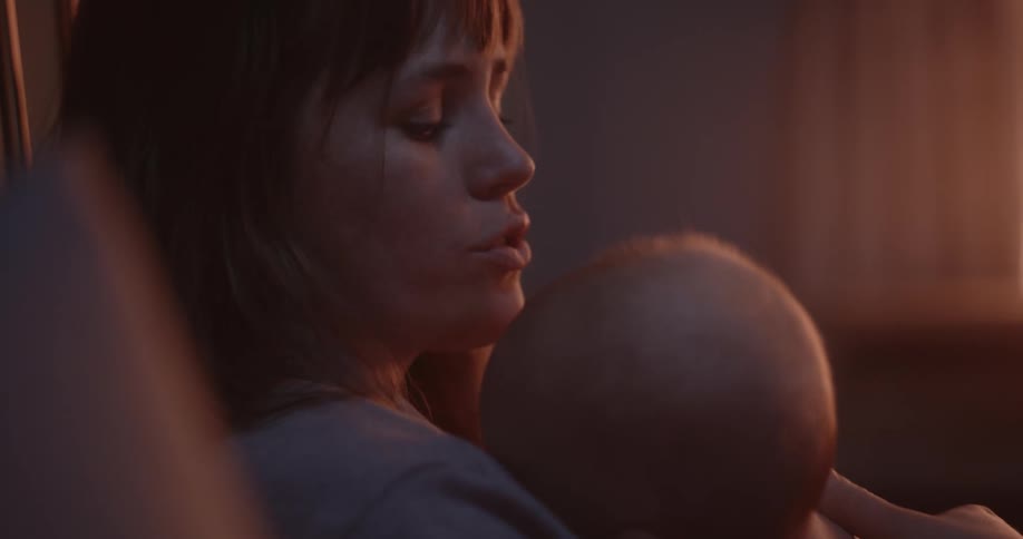 Mother with brown hair rocks newborn baby in her arms in room