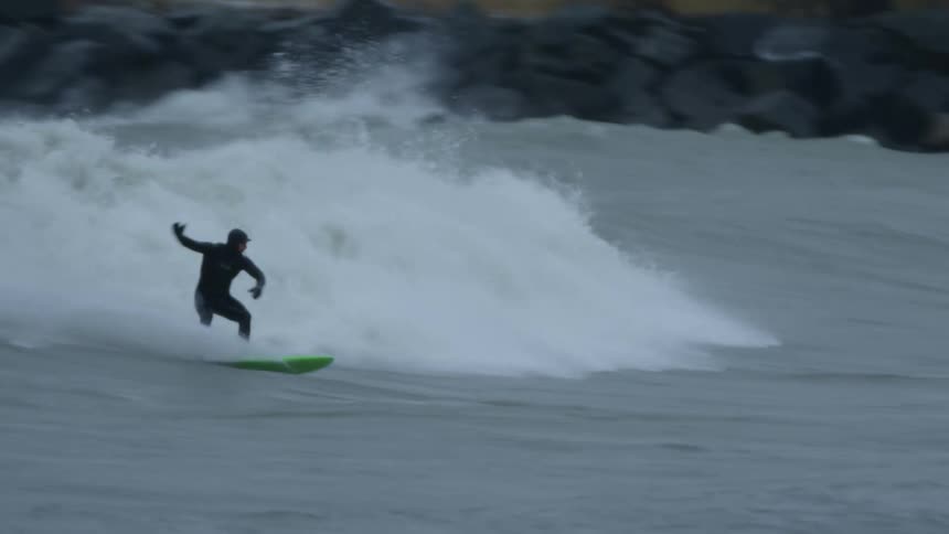 Three surfers wearing wet suits in the ocean one surfing the other two paddling into the wave