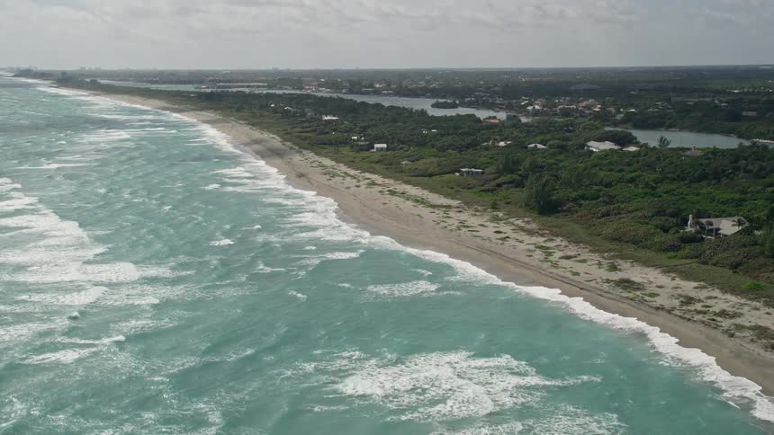 Aerial footage of a beach near residential areas in Hobe Sound Florida showing multiple waves washing ashore