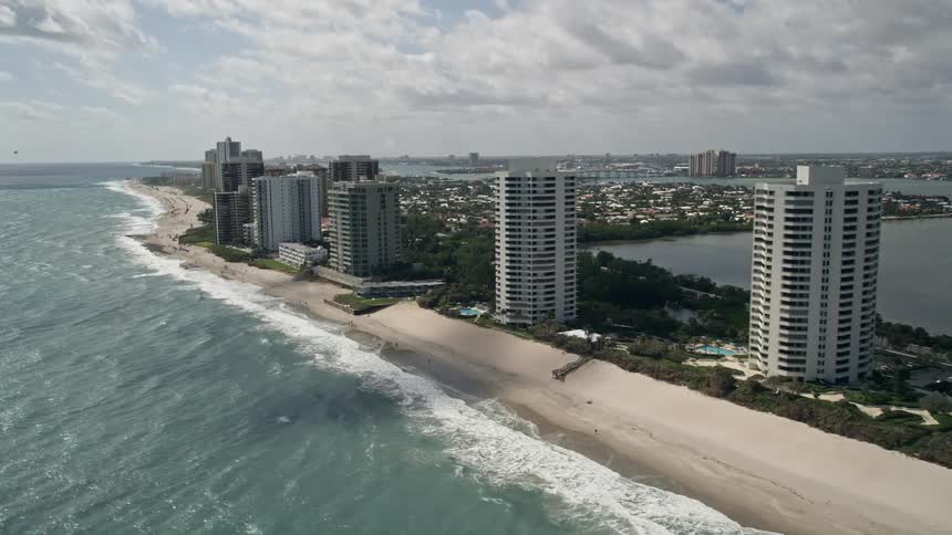 Aerial video footage of beachfront condominium complexes in Riviera Beach Florida with the camera flying past a row of tall buildings located in a coastal city