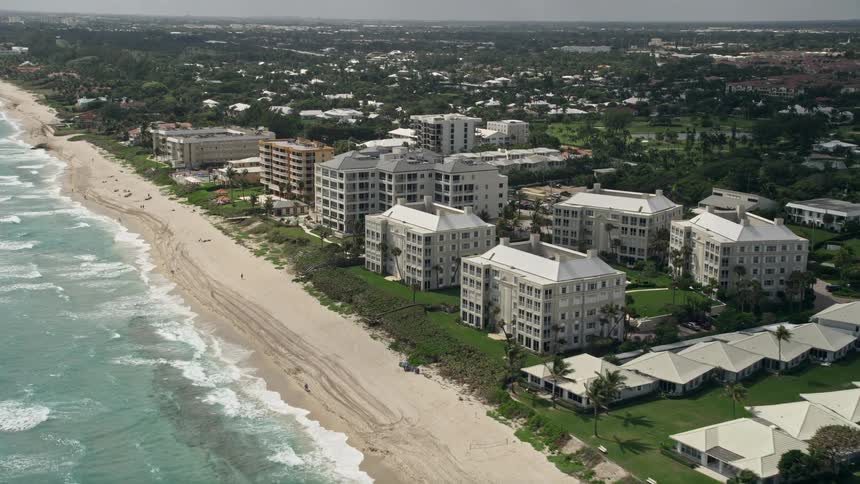 Aerial footage of Delray Beach Florida approaching oceanfront condominiums and a beach with lively beachgoers