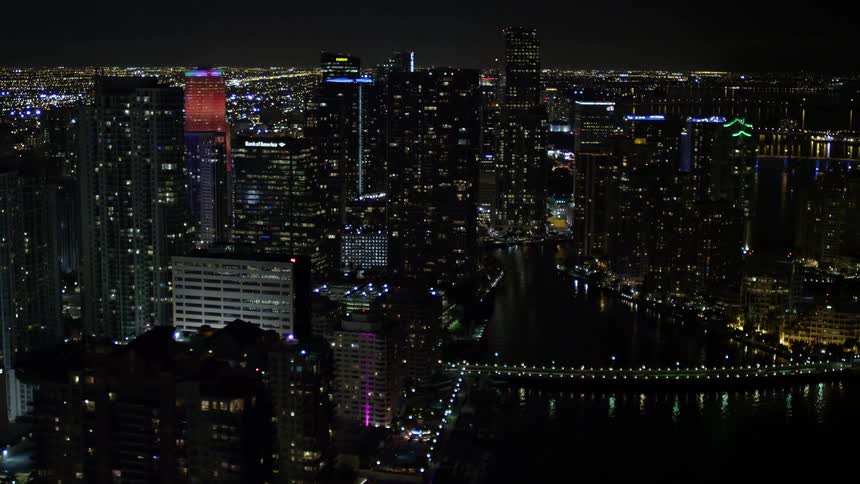 A nighttime aerial view of high rise skyscrapers in downtown Miami and Brickell Key with clear skies and a bridge over the shoreline of Biscayne Bay Florida